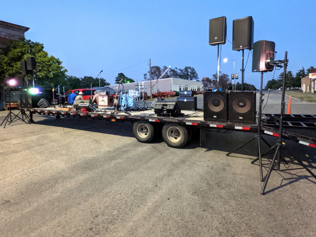 Mobile PA speakers on a trailer stage at an outdoor event at dusk